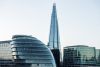 London skyline featuring The Shard rising behind modern glass buildings, including the rounded City Hall structure, under a clear sky.